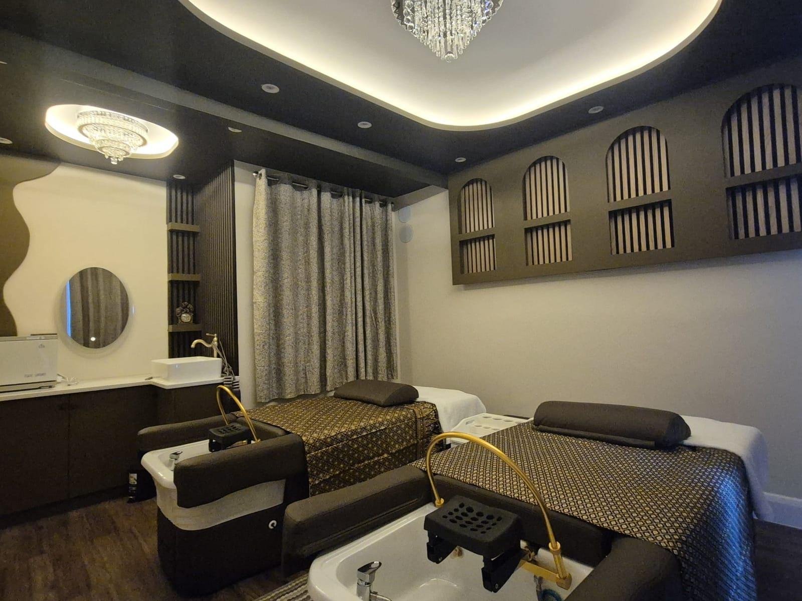 Two head spa beds with basins and gold arched taps, arched wooden wall panels and a crystal chandelier