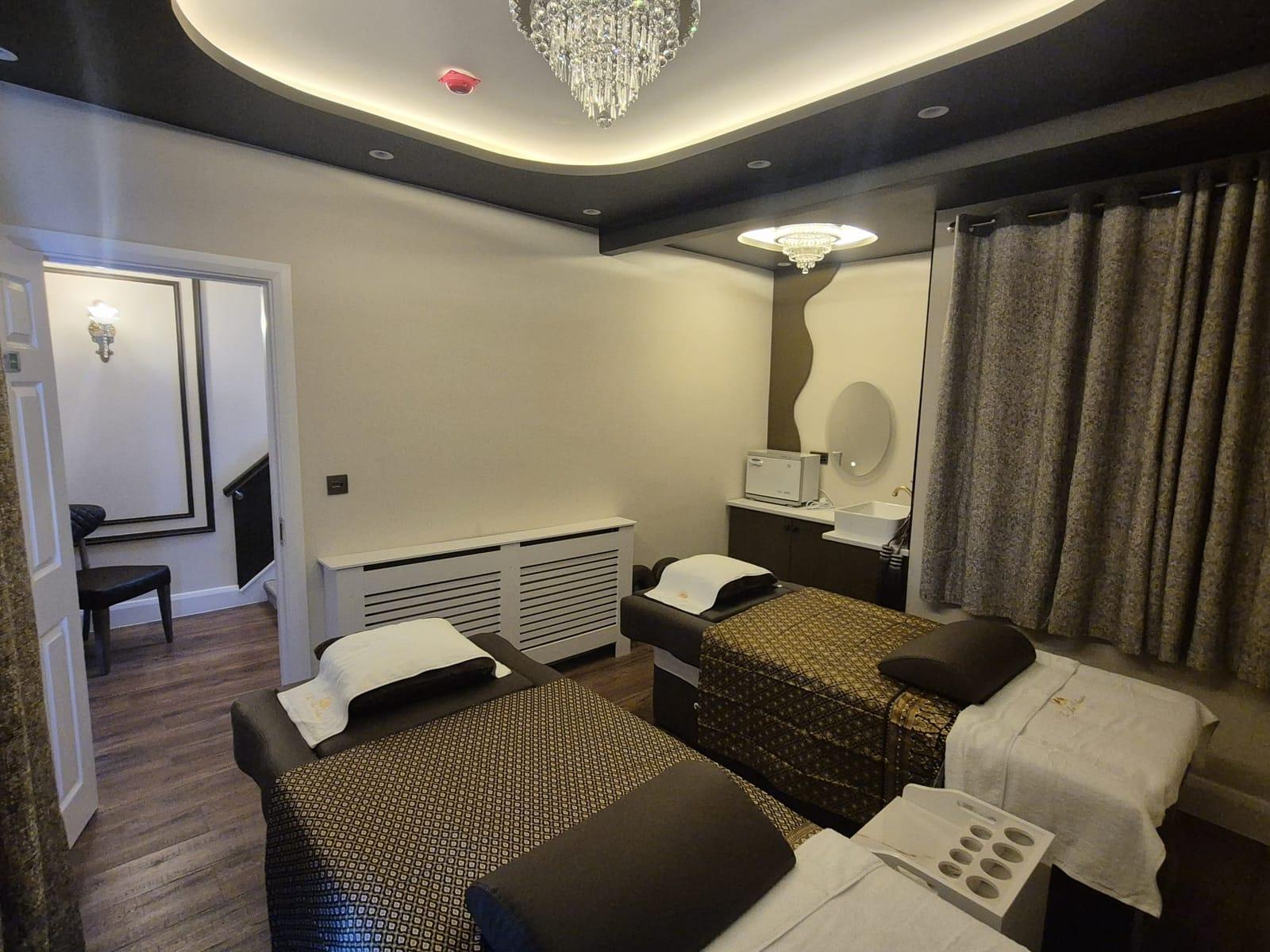 Two massage beds with Thai silk covers and embroidered towels in a room with a glowing ceiling and crystal light