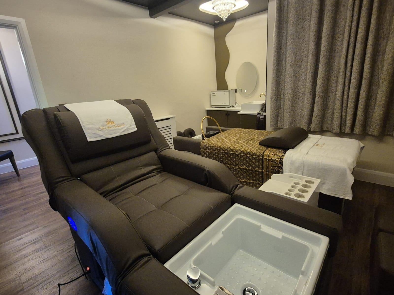 A reclining pedicure chair with a foot basin and an embroidered Skin Ambassador towel