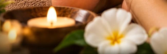 A lit candle in a bowl beside white frangipani flowers