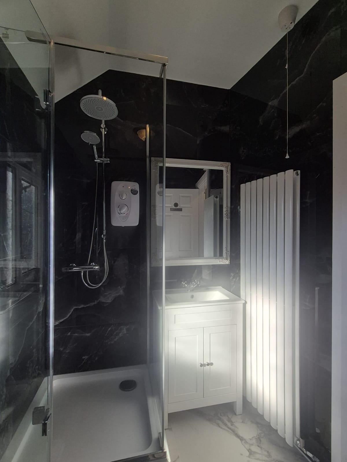 A shower room with black marble-effect walls, a glass shower, a white vanity unit and a tall white radiator
