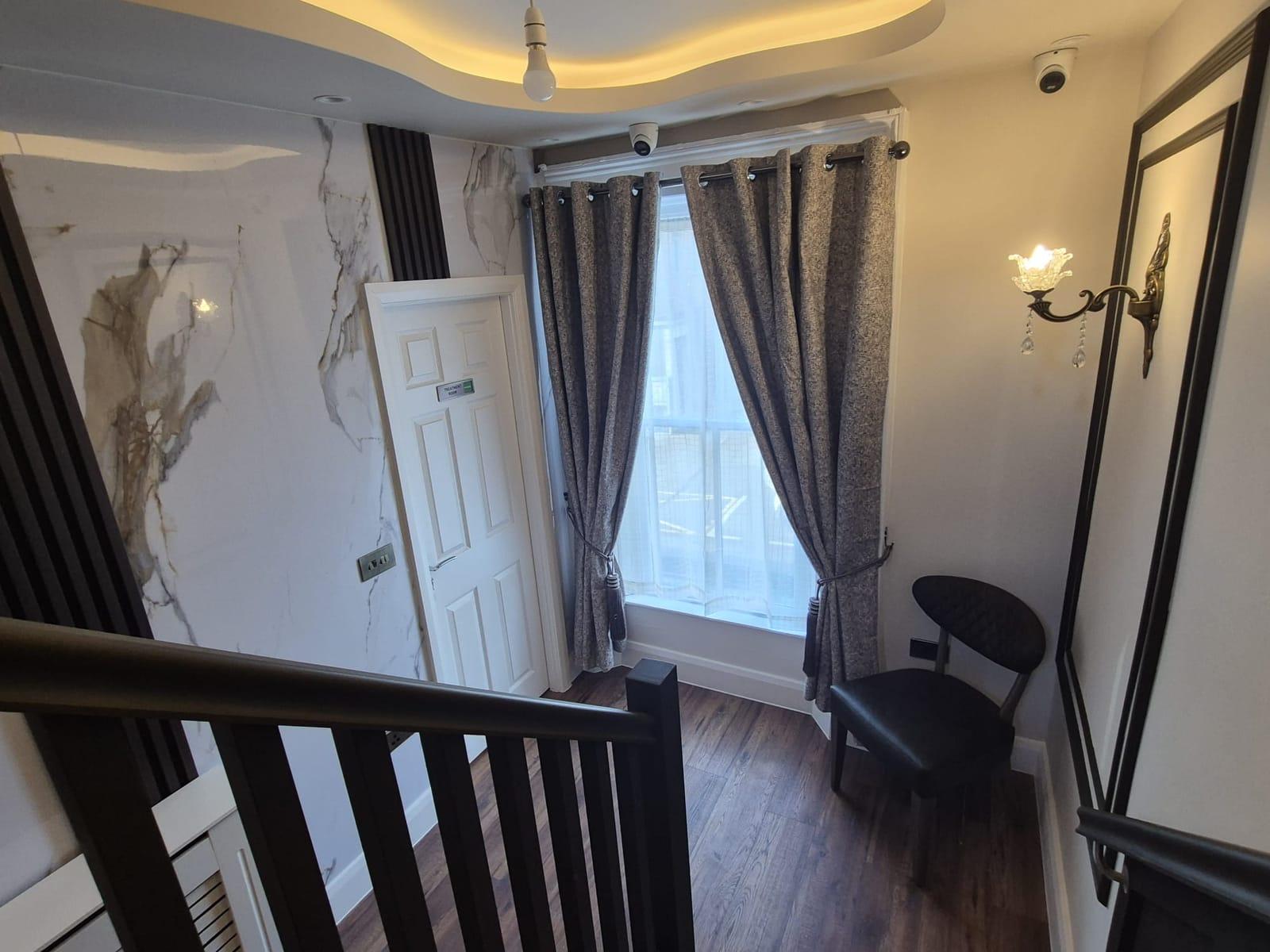 A landing with a white marble-effect wall, a treatment room door, a brass wall light and a dark upholstered chair