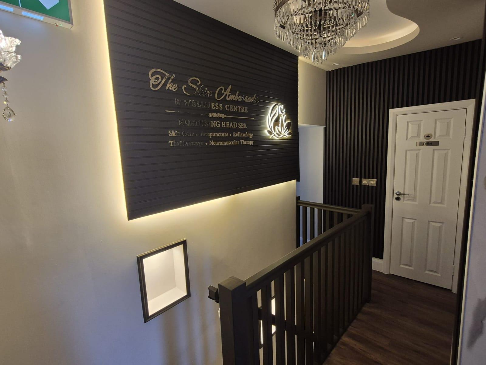 The illuminated Skin Ambassador sign on a dark slatted wall above the staircase, beside a crystal chandelier