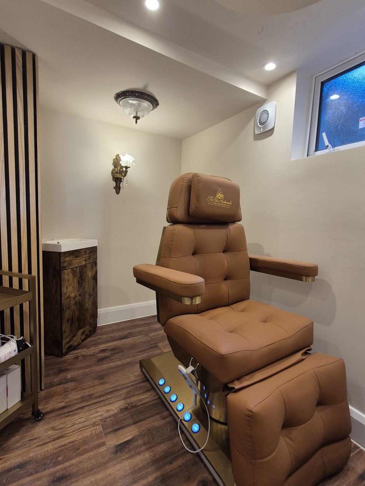 A tan leather treatment chair embroidered with The Skin Ambassador logo beside a wooden basin unit