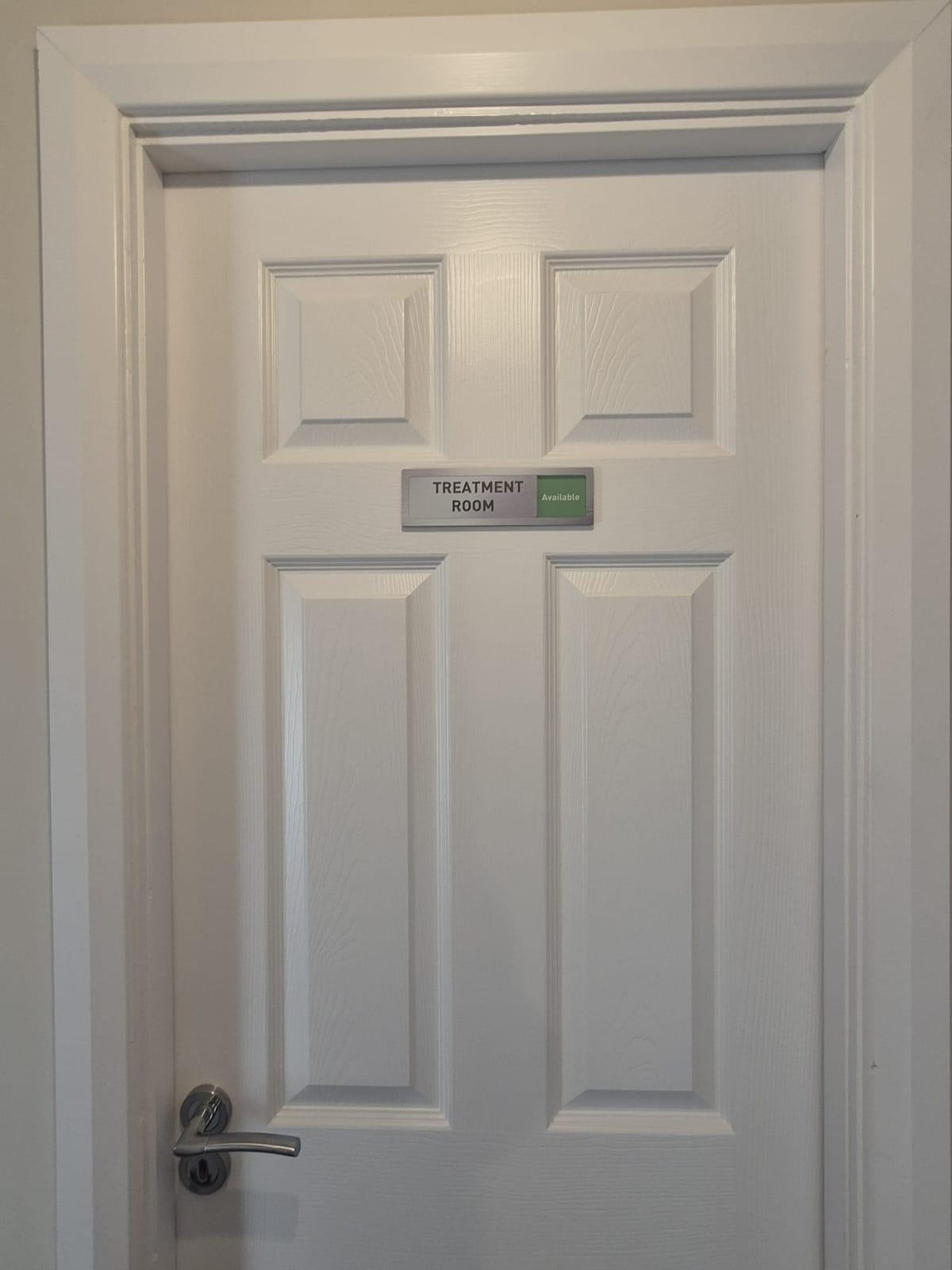 A white panelled treatment room door with a sign showing it is available