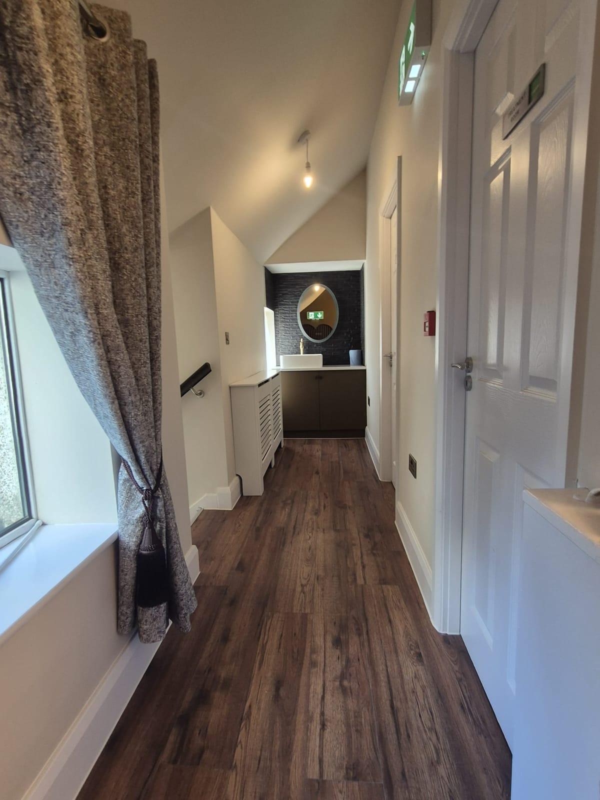 A bright upstairs hallway with wooden flooring leading to a wash basin with an oval mirror
