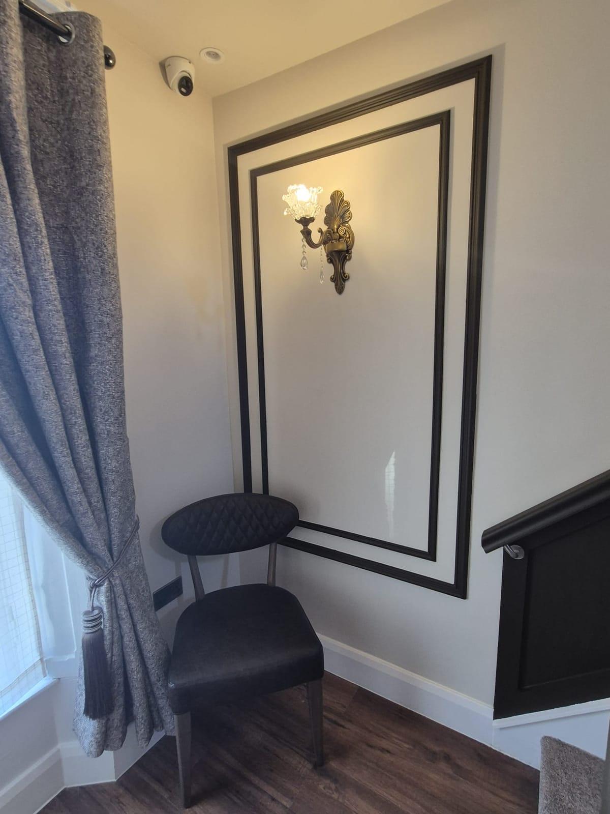 A dark quilted chair beneath a brass and crystal wall light framed by black panel moulding