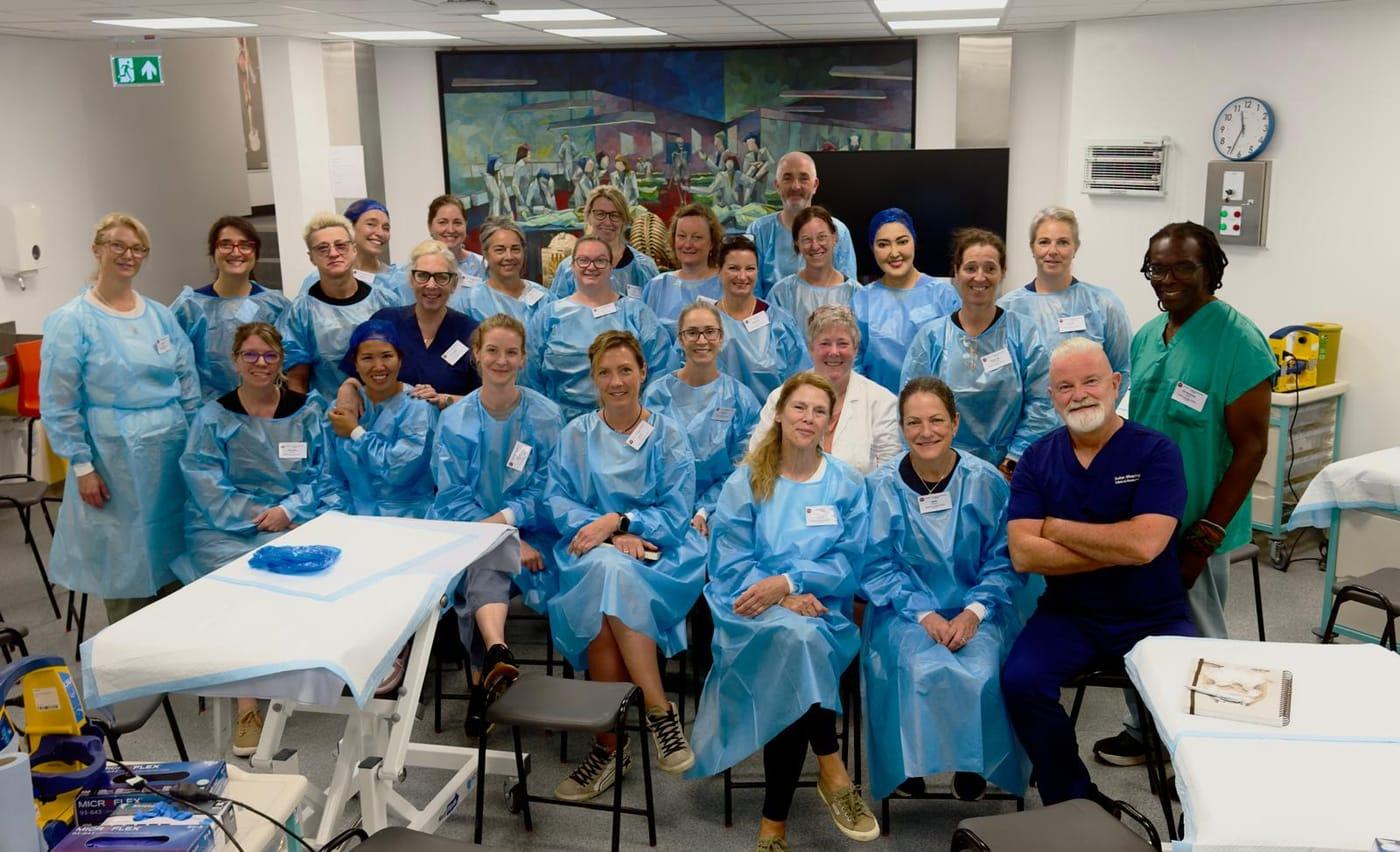 The course group in blue protective gowns gathered in the anatomy laboratory