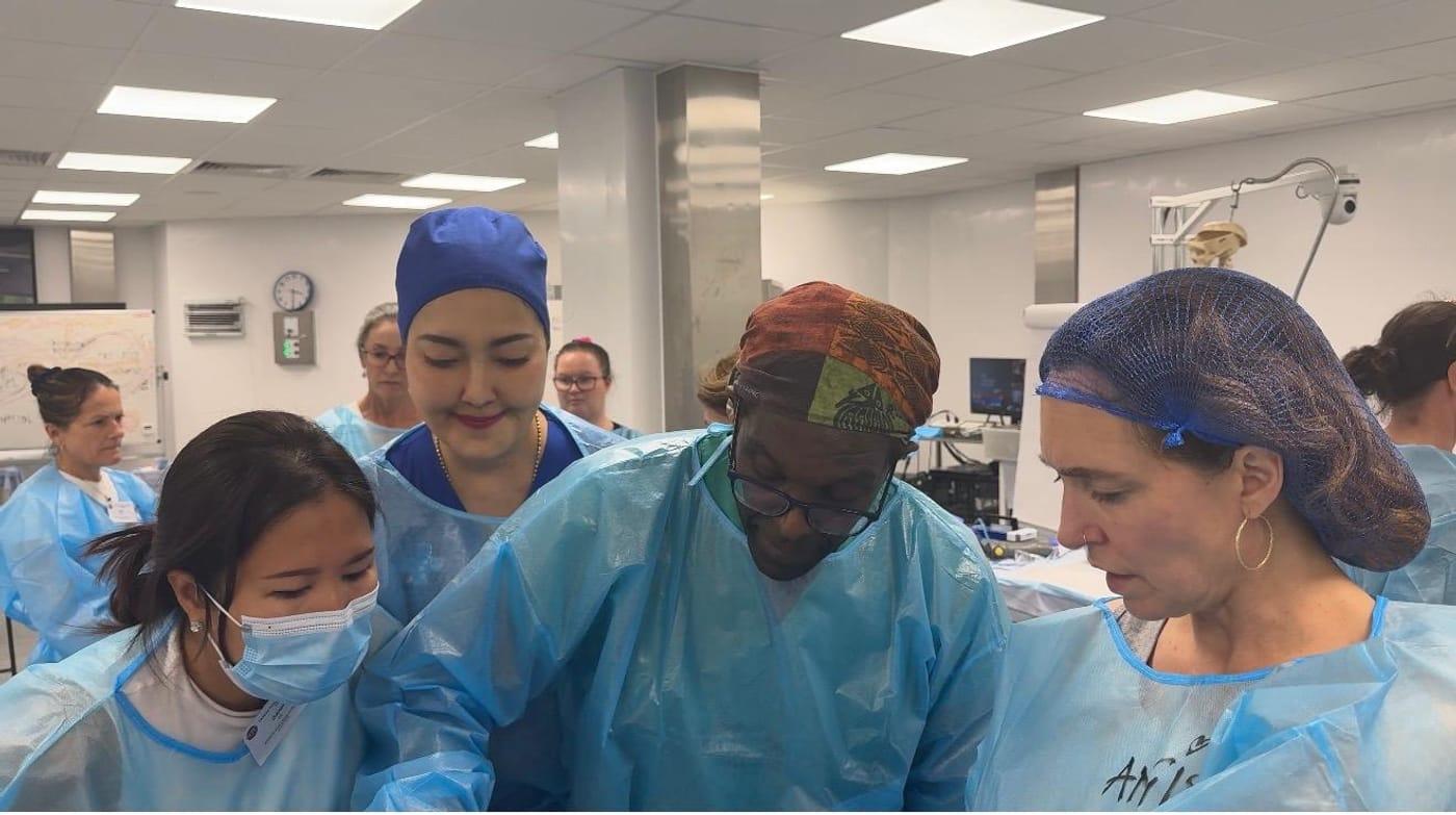 Course members in protective gowns and caps studying anatomy together in the laboratory